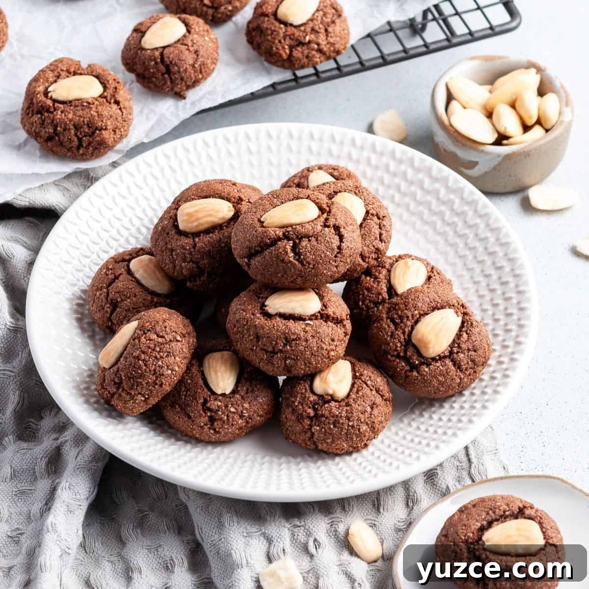 Round white plate with chocolate almond cookies, sitting on a grey cloth.