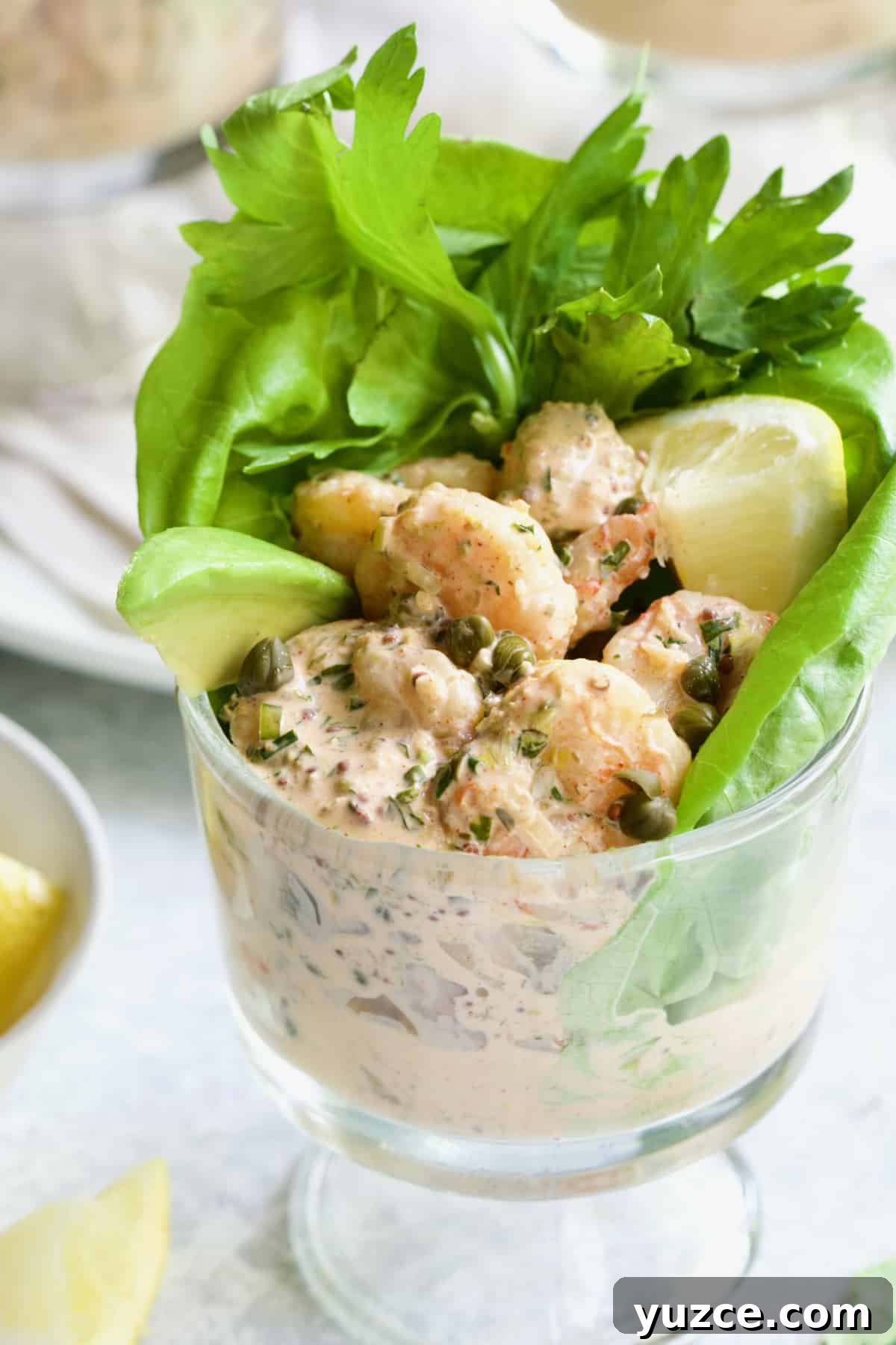 Shrimp Cocktail with Sriracha Remoulade Sauce 7 Sriracha Shrimp Remoulade Cocktail in footed glass with avocado, lemon, lettuce and celery sprigs.