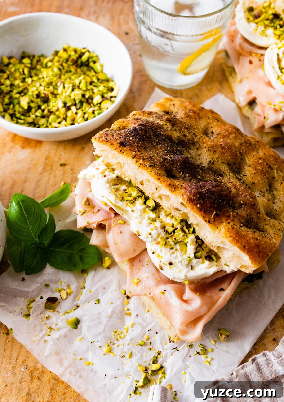 Classic Italian Mortadella Sandwich Recipe — Quick Lunch Idea 3 Assembled Mortadella Sandwich Recipe with Pistachio Pesto and Burrata with pesto on the side. Ready to eat. Lemon water glasses in the background.