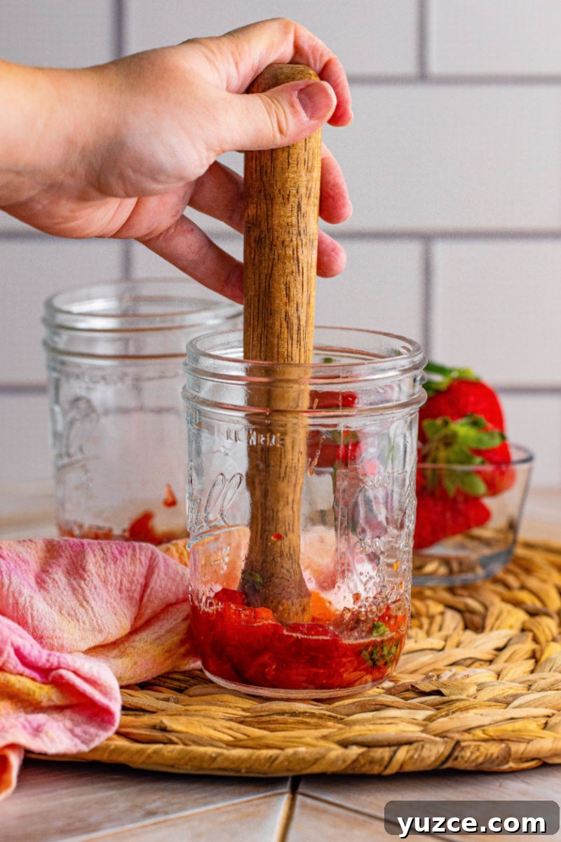 Strawberry Vodka Smash: Refreshing Summer Cocktail Recipe 5 strawberries and mint leaves being muddled in a mason jar