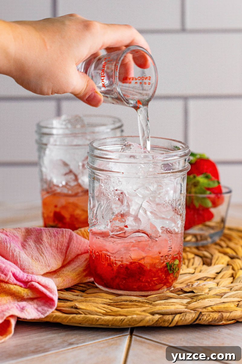 Strawberry Vodka Smash: Refreshing Summer Cocktail Recipe 6 vodka being poured over ice in a glass with muddled strawberries and mint