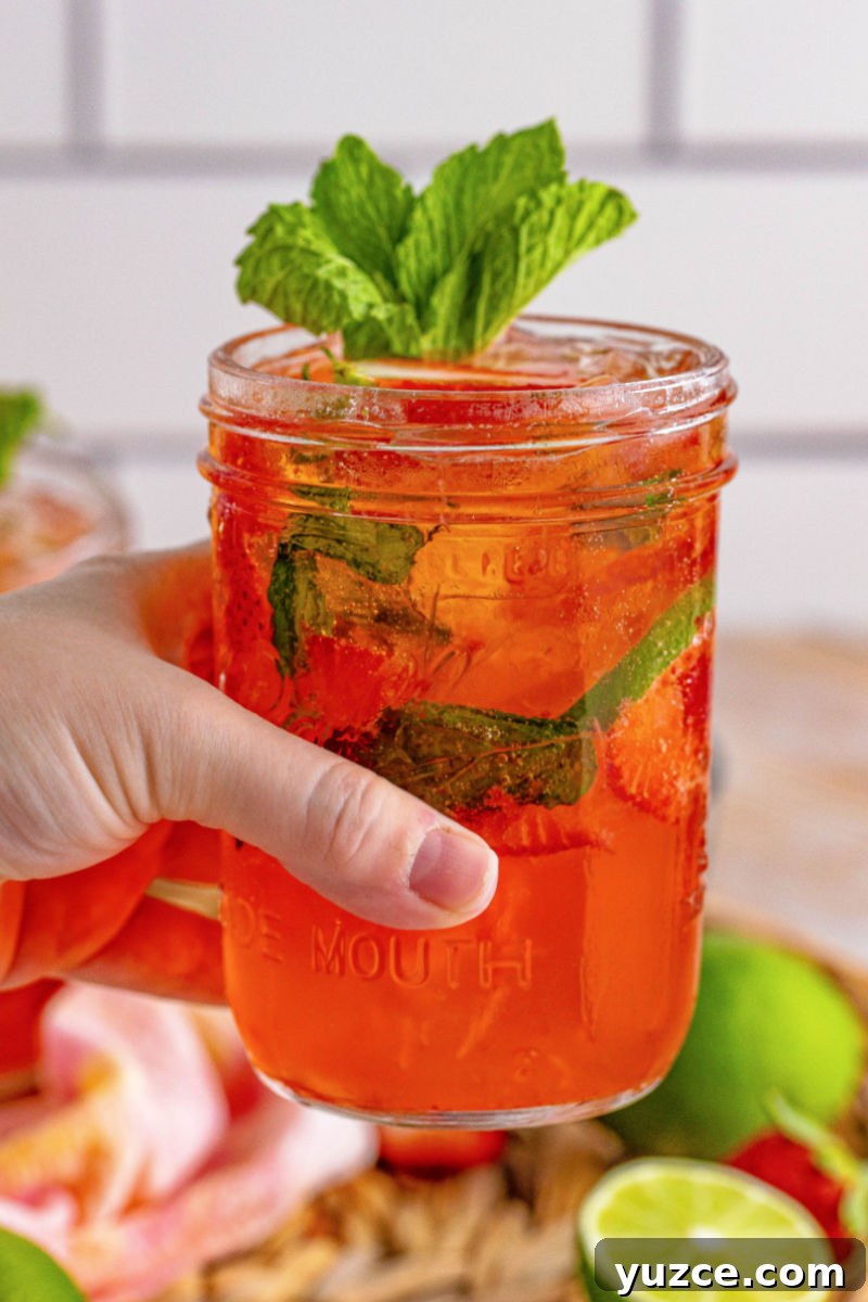 Strawberry Vodka Smash: Refreshing Summer Cocktail Recipe 10 hand holding a mason jar of vodka smash cocktail made with strawberries
