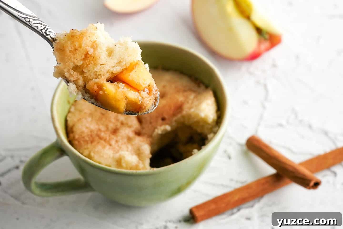 Warm Apple Cinnamon Mug Cake Recipe for One 2 Spoon with apples and cake being held over cake in a green mug
