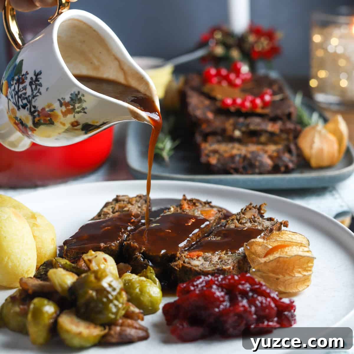 Smoky Roasted Brussels Sprouts with Chestnuts (Vegan) 7 Photo of a plate filled with 3 slices of this vegan nut roast, some roast potatoes, sprouts, cranberry sauce, and a pretty jug pouring gravy over the top, with the full vegan nut roast in the background.