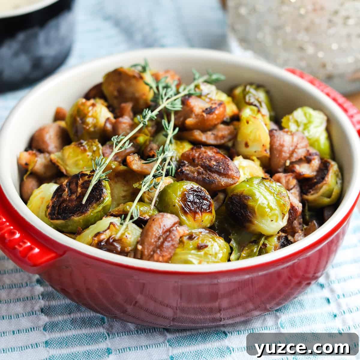 Smoky Roasted Brussels Sprouts with Chestnuts (Vegan) 8 Photo of Christmas roast brussels sprouts with chestnuts in a red bowl on a tablecloth with tablescape in the background.