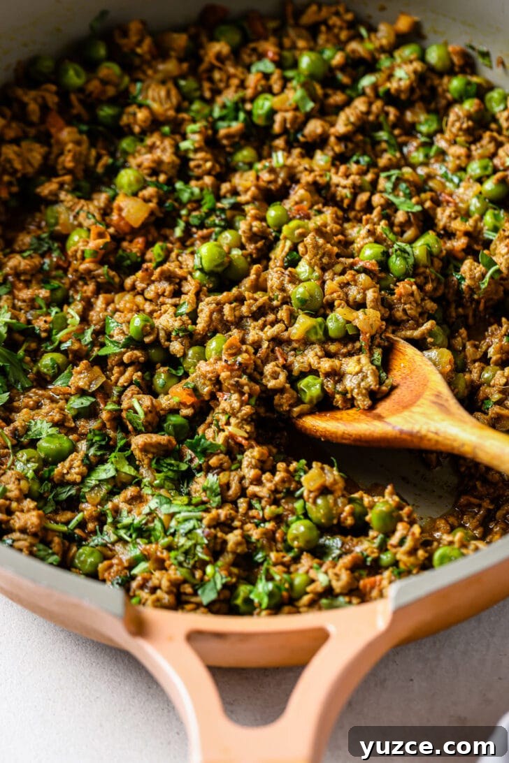 Keema Matar: Spiced Ground Beef and Pea Curry Recipe 10 Close up of a skillet of Keema Matar with a wooden spoon.