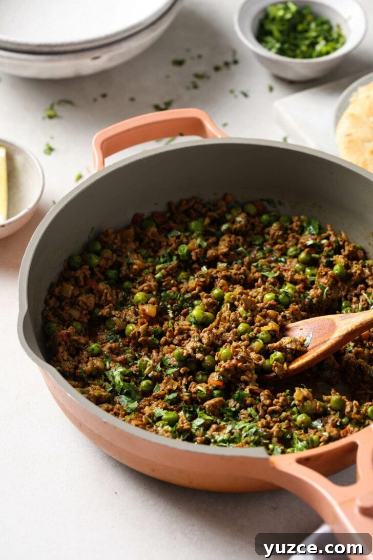 Keema Matar: Spiced Ground Beef and Pea Curry Recipe 11 Keema Matar in a skillet with a wooden spoon.