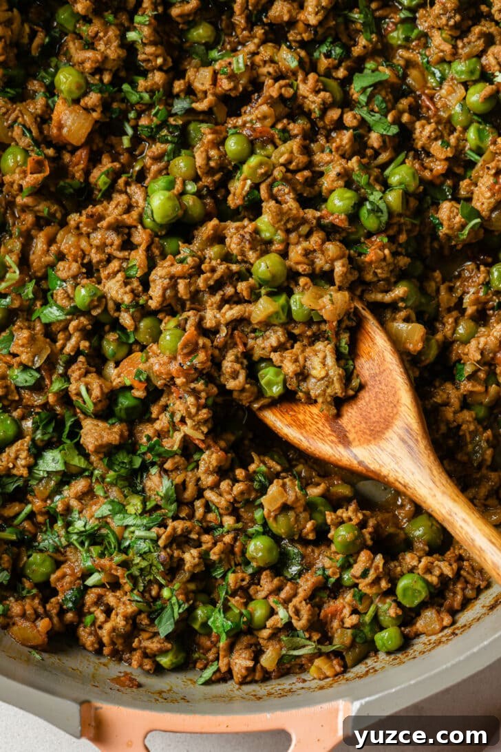Keema Matar: Spiced Ground Beef and Pea Curry Recipe 3 Close up of Keema Matar in a skillet with a wooden spoon.