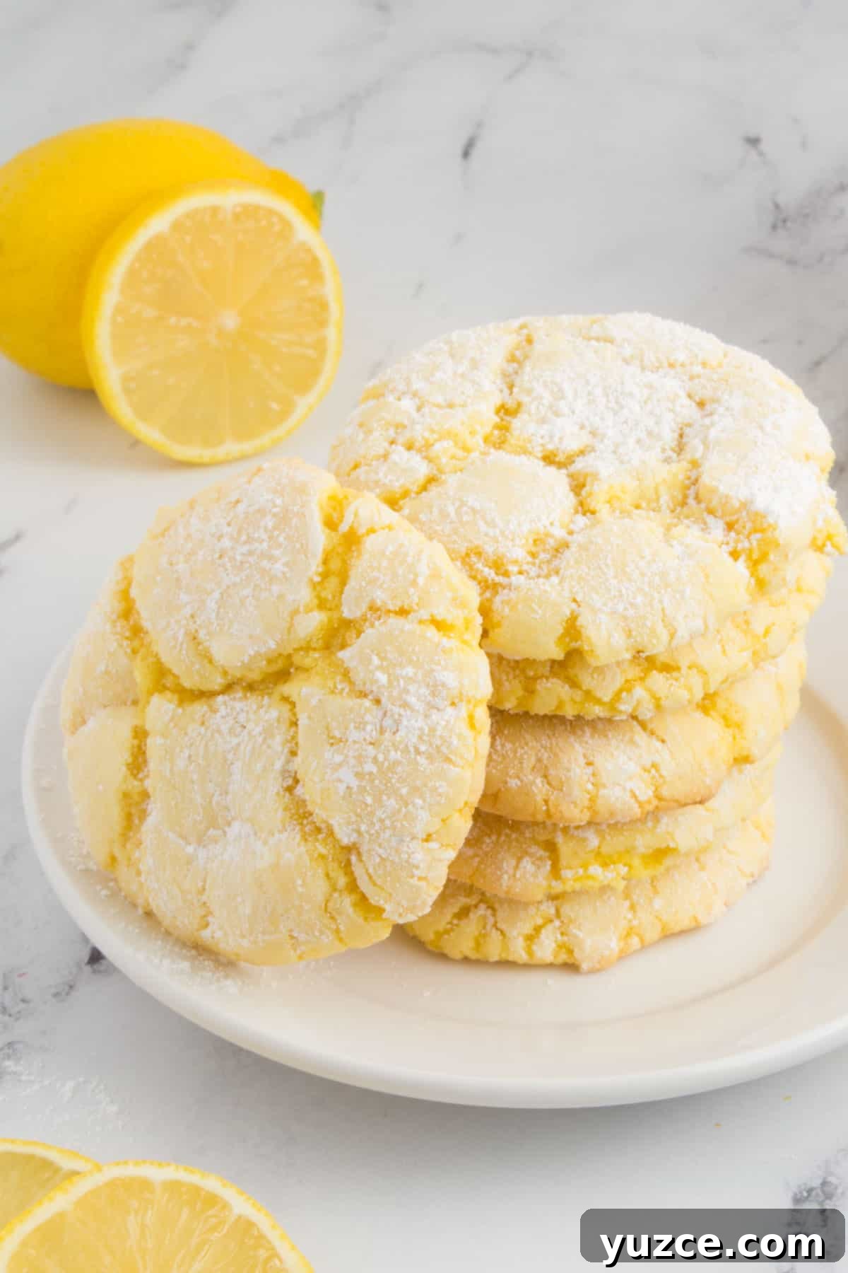 Chewy Lemon Cake Mix Cookies: Quick Citrus Cookie Recipe 11 lemon cookies arranged on a white plate sitting on a granite countertop with sliced lemons around the plate