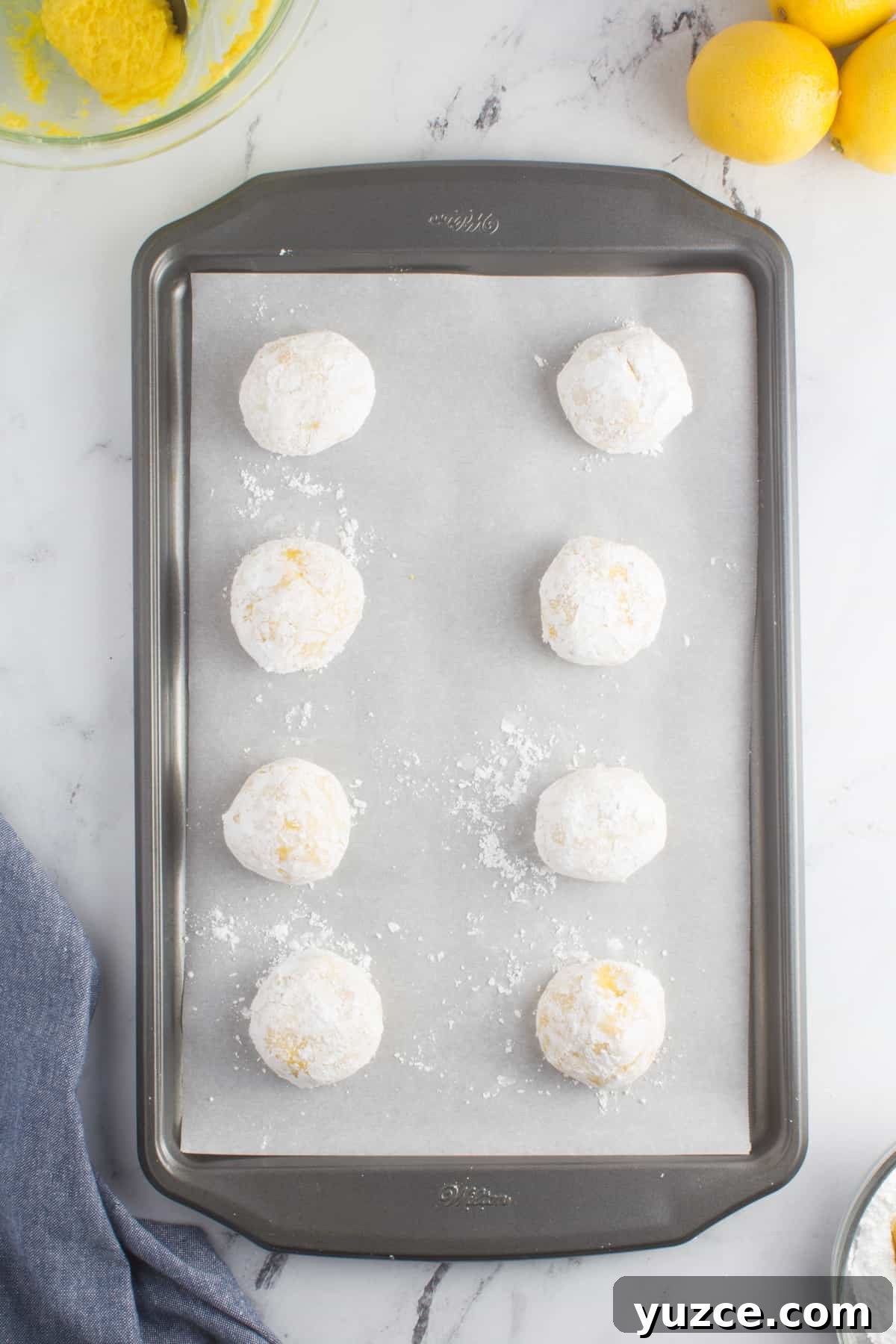 Chewy Lemon Cake Mix Cookies: Quick Citrus Cookie Recipe 8 lemon cookie dough balls coated in powdered sugar sitting on a baking sheet lined with parchment paper