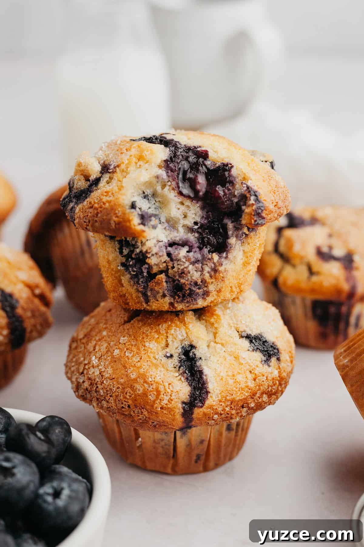 Bakery-Style Buttermilk Blueberry Muffins Recipe 6 Two muffins stacked on top of each other, the muffin on top has a bite taken out of it.