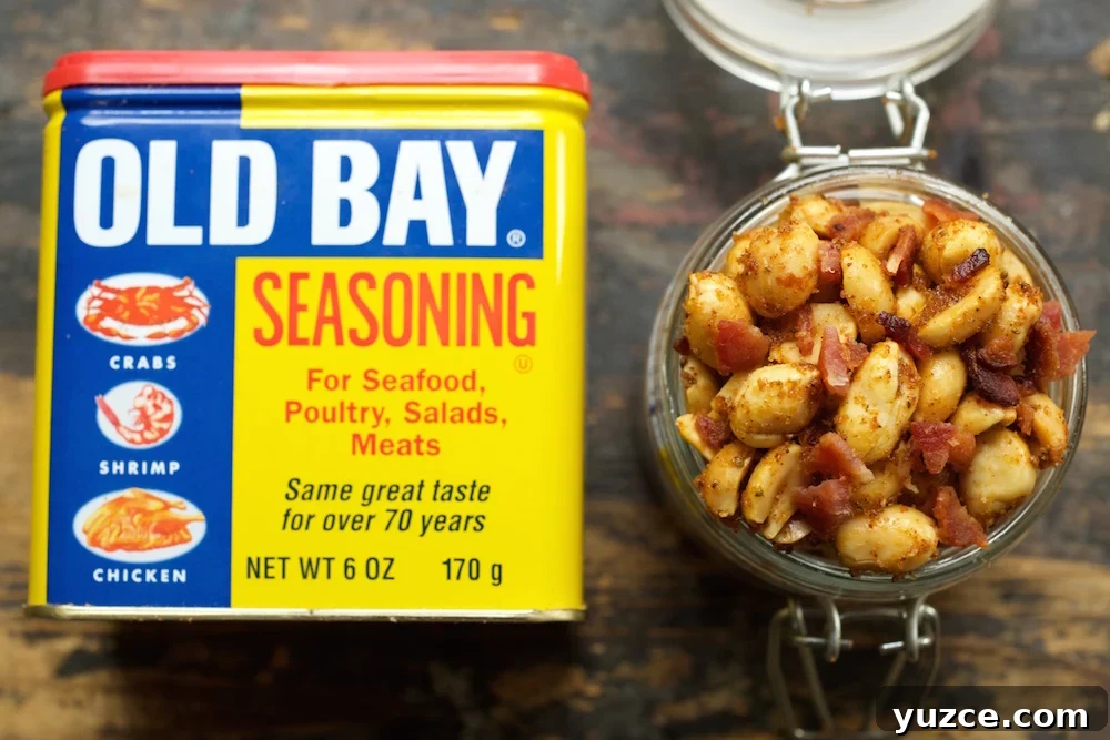 Savory Old Bay Spiced Peanuts — Crunchy Snack Recipe 4 Overhead look at a glass jar filled to the top with Old Bay & bacon peanuts next to a can of old bay seasoning.