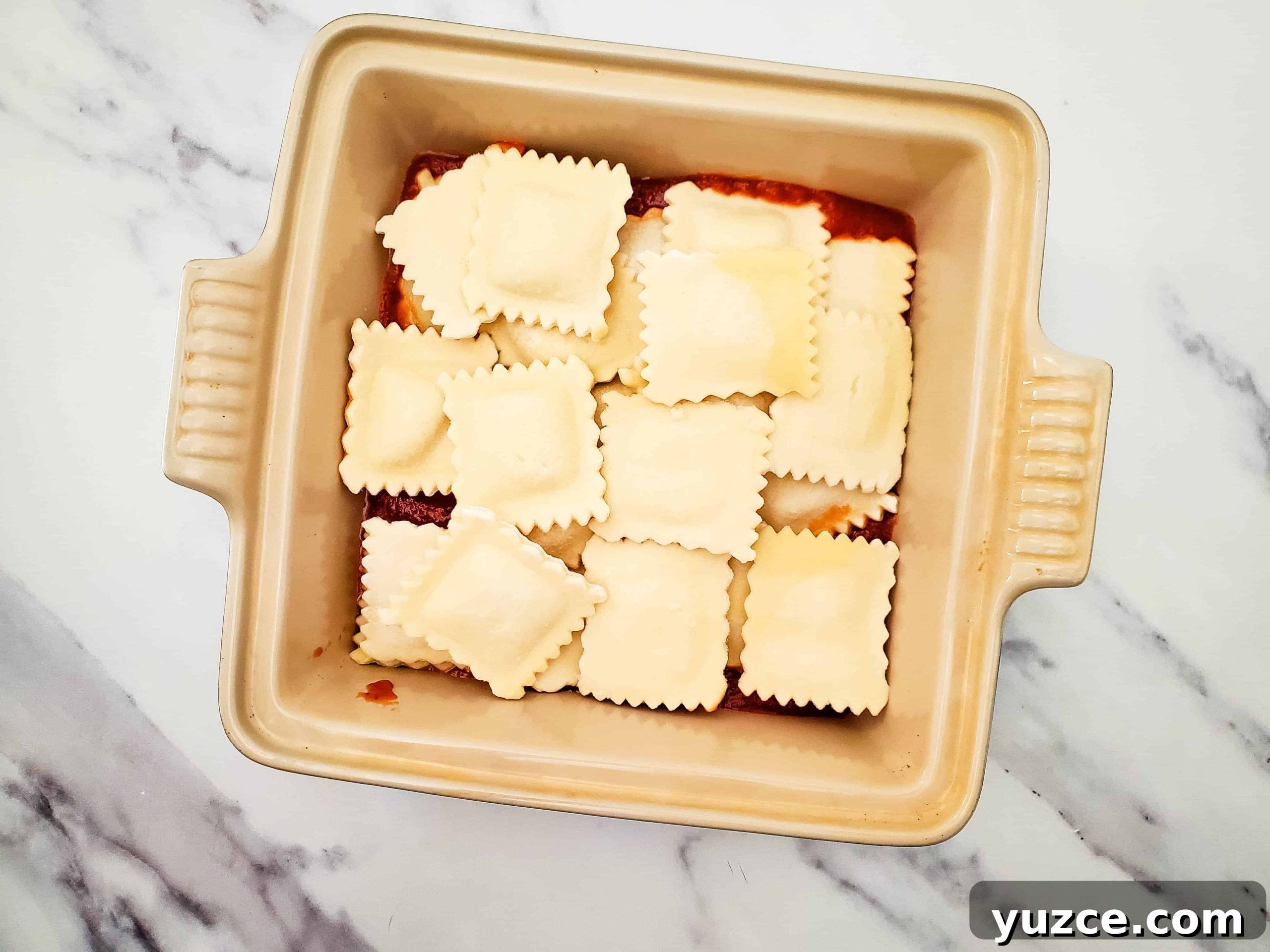 Quick Ravioli Lasagna Recipe for Busy Weeknight Dinners 5 Glass baking dish with pasta sauce and frozen ravioli on top of a white counter