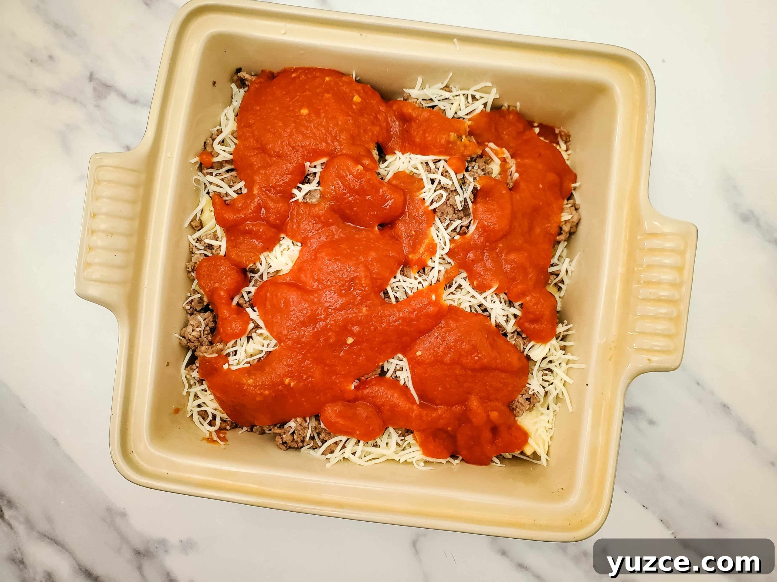 Quick Ravioli Lasagna Recipe for Busy Weeknight Dinners 7 Casserole baking dish with layered frozen ravioli recipe and pasta sauce on top of a marble counter