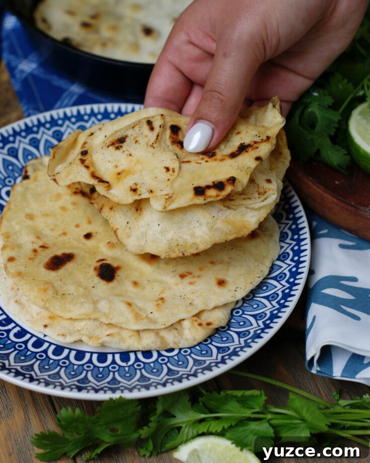 A woman picking up a fresh, warm flour tortilla to show how soft and tender they are.