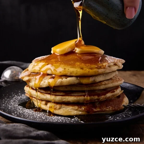 A stack of six fluffy pancakes with butter and syrup.