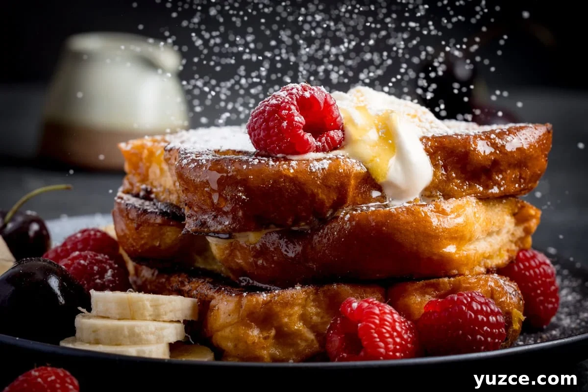 Close-up of caramelised French toast slices topped with whipped cream, raspberries, banana slices, and icing sugar being sprinkled, served on a black plate.