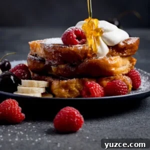 A stack of brioche French toast topped with whipped cream, raspberries, banana slices, and cherries, with syrup being poured over the top.