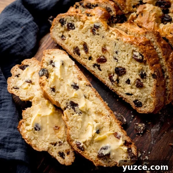 Sliced fruit soda bread with butter rests on a wooden surface.