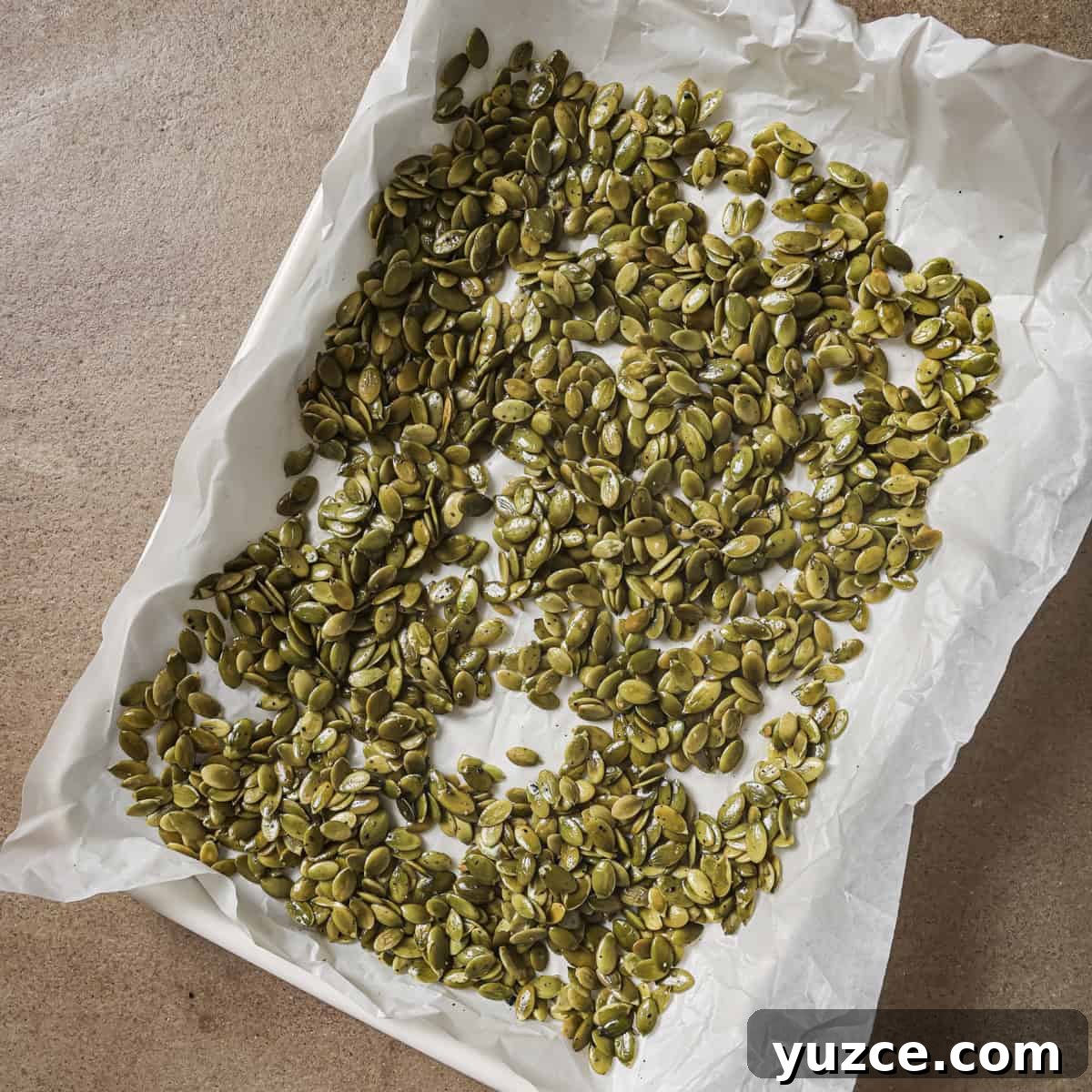 Crispy Oven-Roasted Pepitas with Sea Salt 9 unroasted pepitas on a parchment paper lined sheet pan.