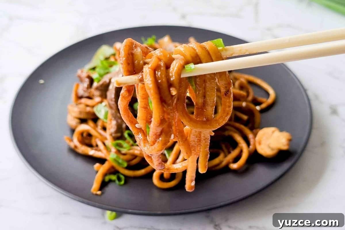 Beef Noodle Stir-Fry with Garlic and Sesame Sauce 11 Close up of cooked noodles being held up by a pair of chopsticks