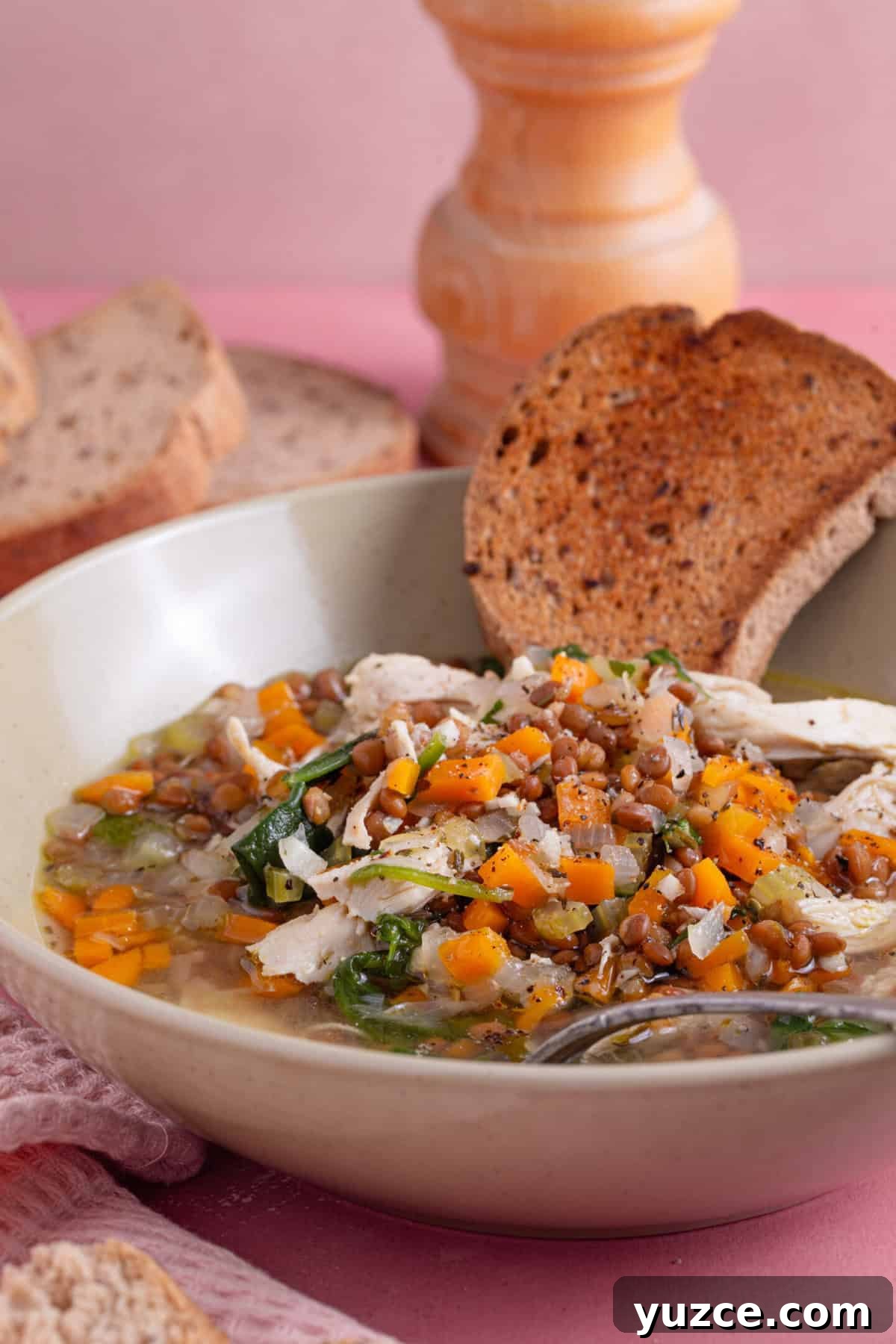 Hearty Chicken and Lentil Soup Recipe for Cozy Weeknights 3 A bowl of chicken and lentil soup with a slice of brown gluten free bread dipped in the side.