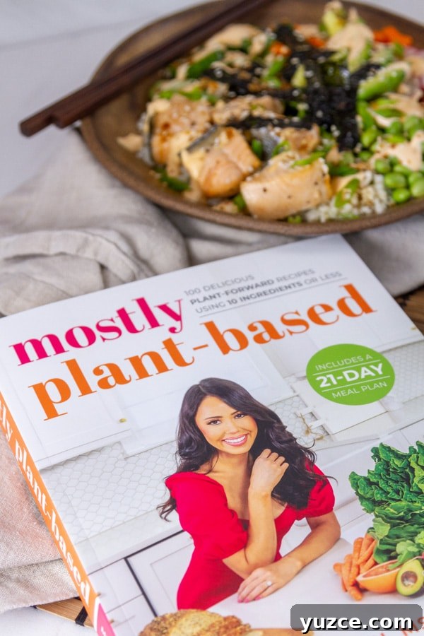Grilled Salmon Bowl with Quinoa, Avocado & Citrus Dressing 5 the cookbook and nutrition book "Mostly Plant-Based" in front of a sushi bowl.