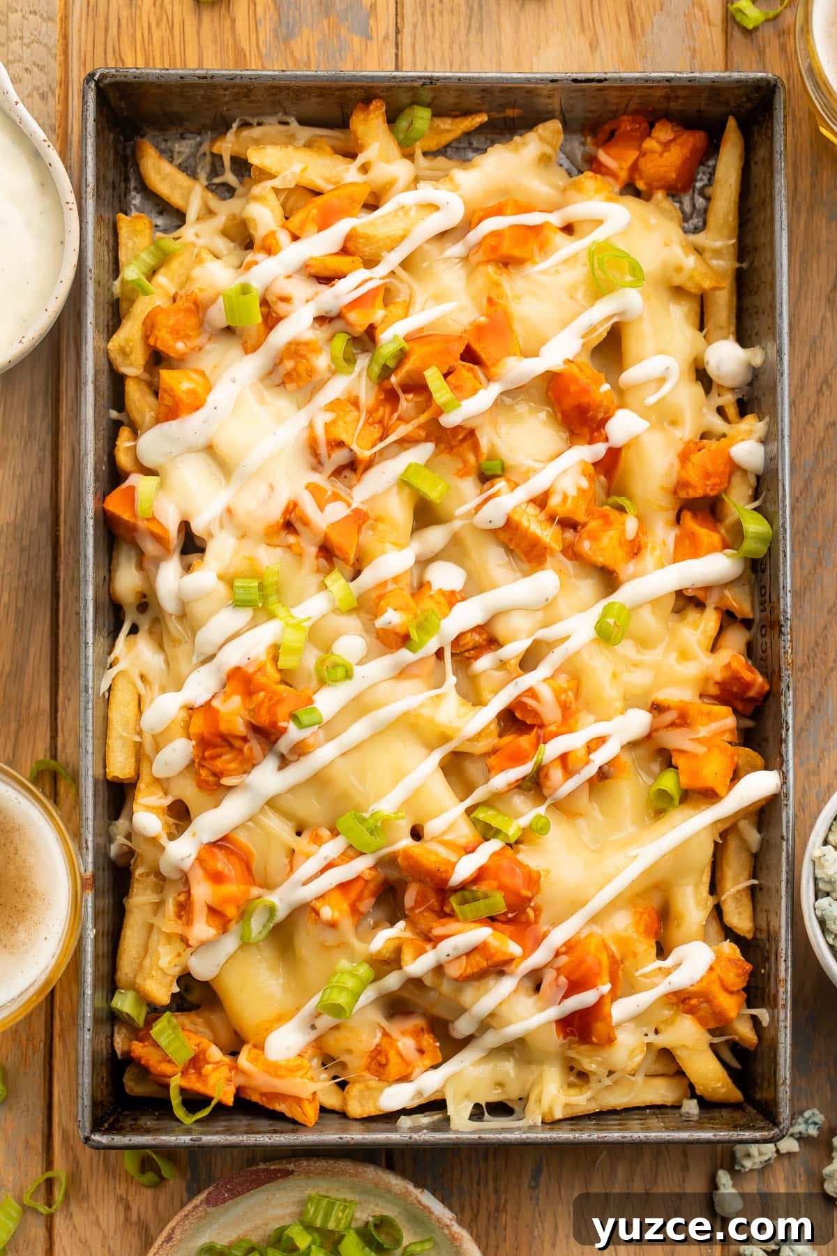 Crispy Buffalo Chicken Fries Recipe with Tangy Ranch Dip 2 Overhead view of a rectangular baking pan holding french fries topped with buffalo chicken, green onions, and a ranch dressing drizzle.