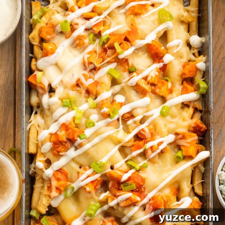 Crispy Buffalo Chicken Fries Recipe with Tangy Ranch Dip 4 Overhead view of a rectangular baking pan holding french fries topped with buffalo chicken, green onions, and a ranch dressing drizzle.