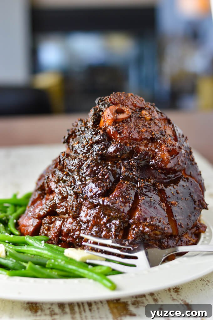 Brown Sugar and Whole Grain Mustard Glazed Baked Ham 2 A cooked glazed ham sitting on a white platter, a large serving fork sits next to it along with a side of green beans.