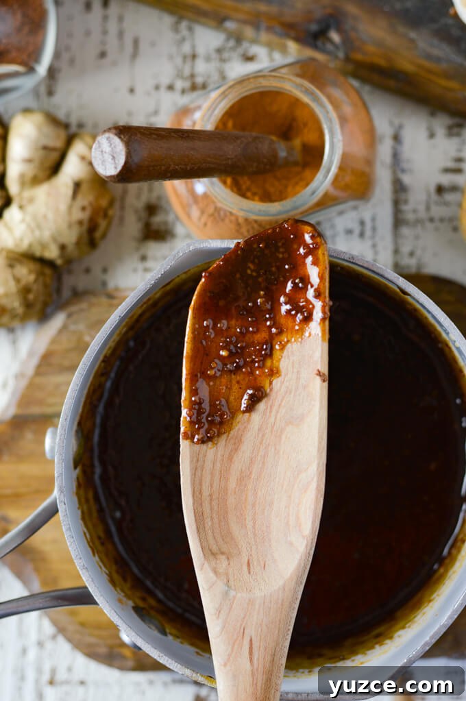 Brown Sugar and Whole Grain Mustard Glazed Baked Ham 6 A wooden spoon with brown sugar glaze sits on a pan of the same glaze. A jar of cinnamon spice and fresh ginger sit next to it.