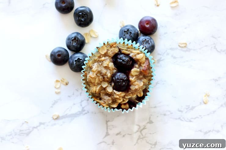 Baked blueberry oatmeal cupcake sitting on a white table with blueberries and oats.