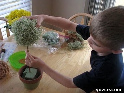 Spring Topiary Ideas to Refresh Your Garden Today 8 child placing styrofoam ball on top of wooden dowel