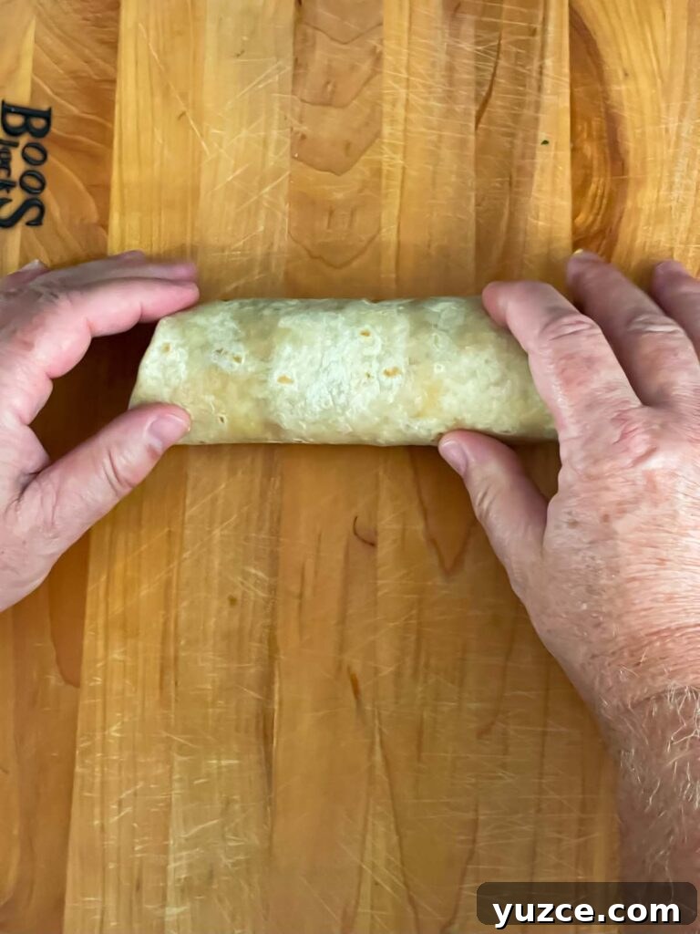 Crispy Baked Chicken Chimichangas with Cheesy Filling 8 Wrapped chimichango on a wooden board.