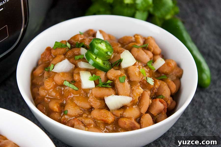 Ninja Foodi Mexican pinto beans (charro beans) in a white bowl with a jalapeno and onion garnish.