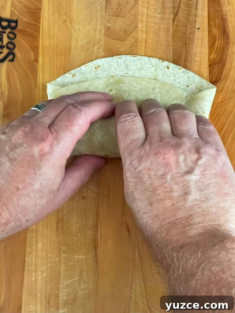 Crispy Baked Chicken Chimichangas with Cheesy Filling 7 Wrapping the tortilla on a wooden board.