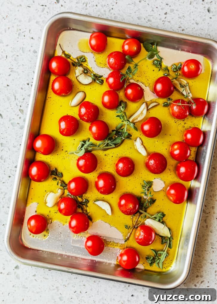 Baked Caprese Crostini with Fresh Basil Pesto 4 A sheet pan of tomatoes, oil, and herbs on a white terrazzo counter.