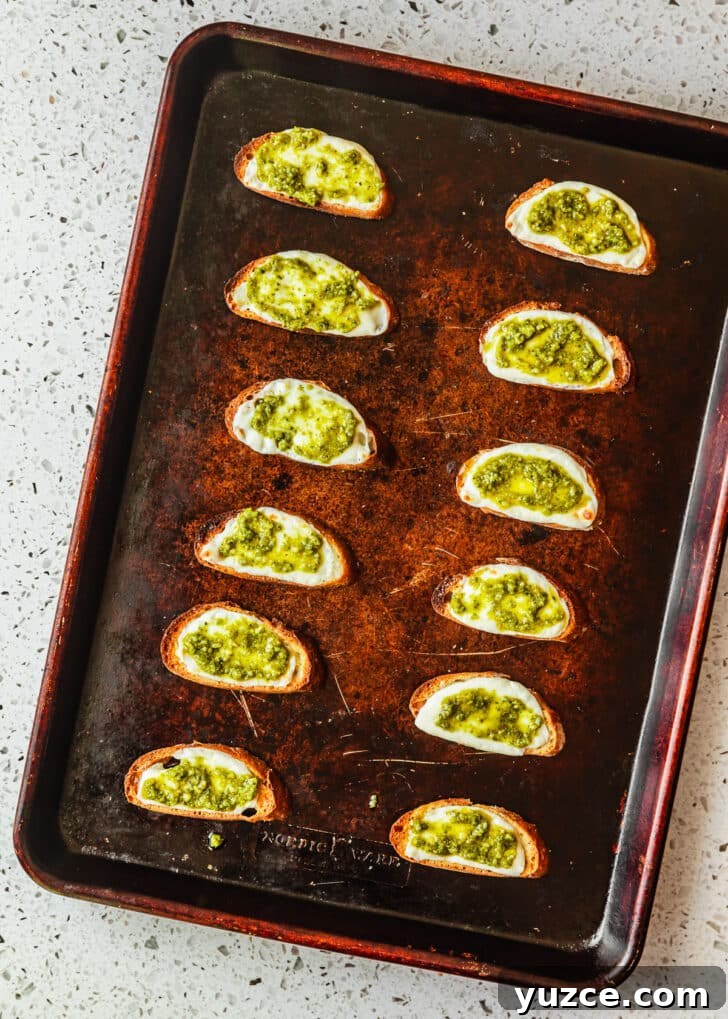 Baked Caprese Crostini with Fresh Basil Pesto 8 A sheet pan of crostini with mozzarella and pesto on a white terrazzo counter.