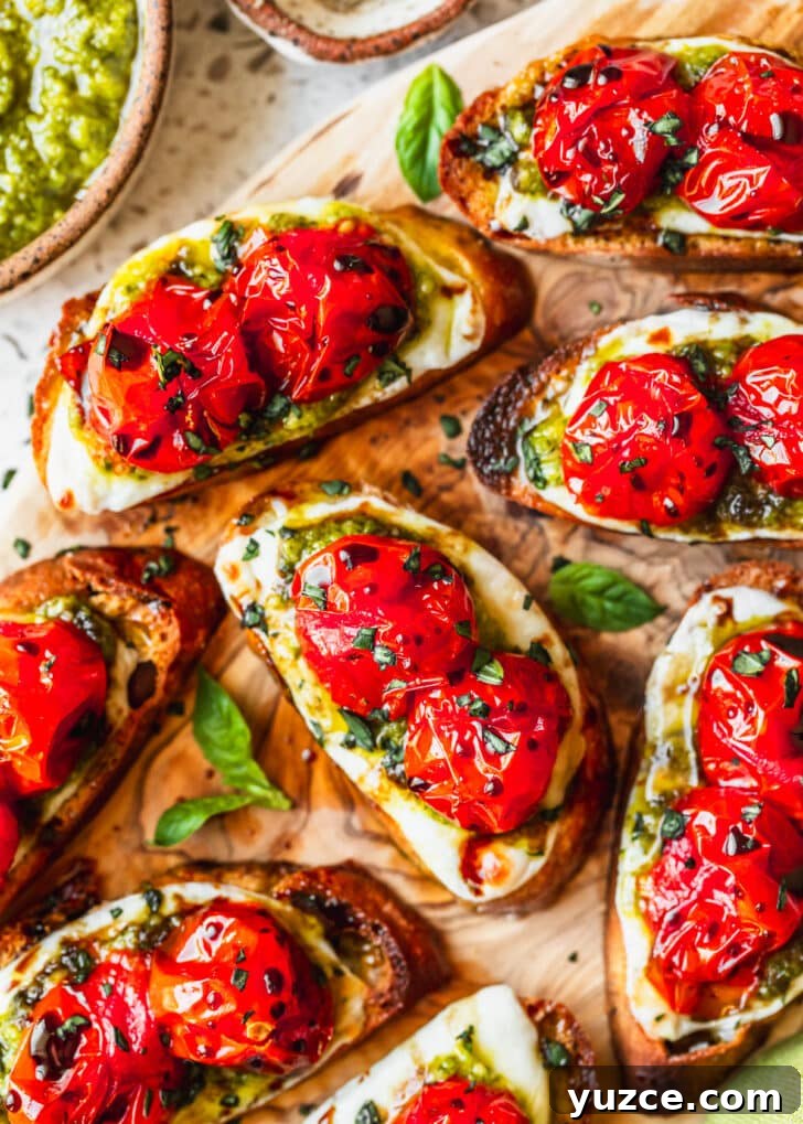 Baked Caprese Crostini with Fresh Basil Pesto 9 Rows of roasted Caprese crostini on a wood board next to a brown bowl of pesto with a white background.