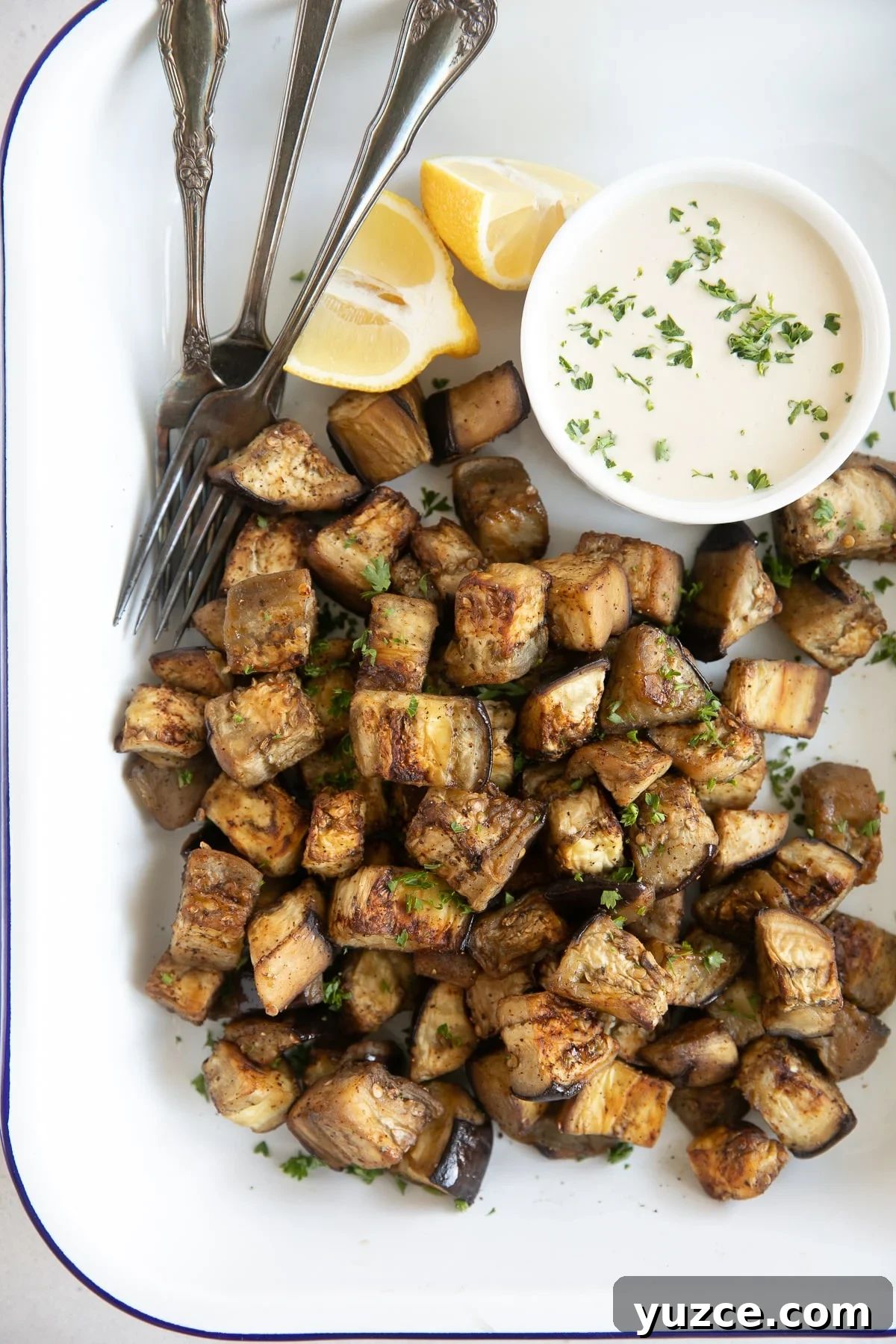 Crispy Oven-Roasted Eggplant with Garlic and Herbs 2 Image of a white tray filled with golden roasted eggplant garnished with chopped parsley.