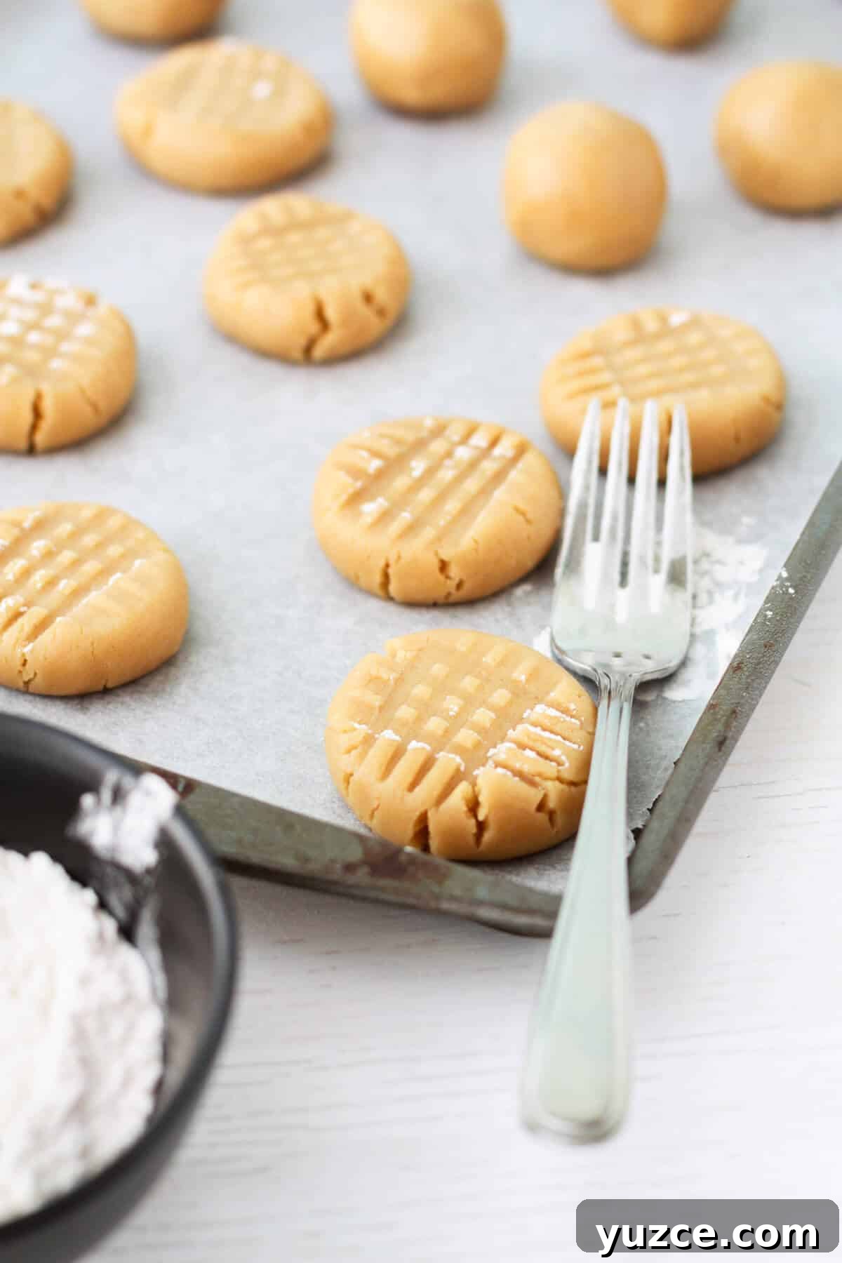 Classic Peanut Butter Cookies Made with Natural Peanut Butter 12 Pressing scoops of peanut butter cookie dough with a fork before baking.