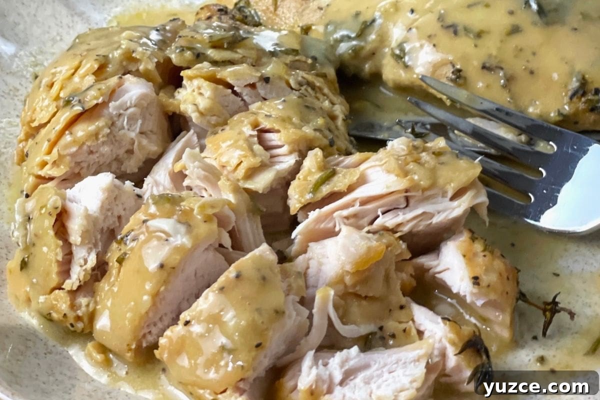 13 Crockpot Thanksgiving Recipes to Save Oven Space 4 A close-up of sliced chicken breast topped with a creamy herb sauce on a plate with a fork.