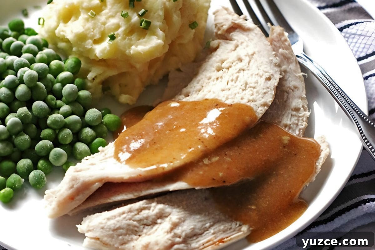 13 Crockpot Thanksgiving Recipes to Save Oven Space 8 A plate of sliced roast turkey covered in brown gravy, accompanied by mashed potatoes with chives and a serving of green peas.