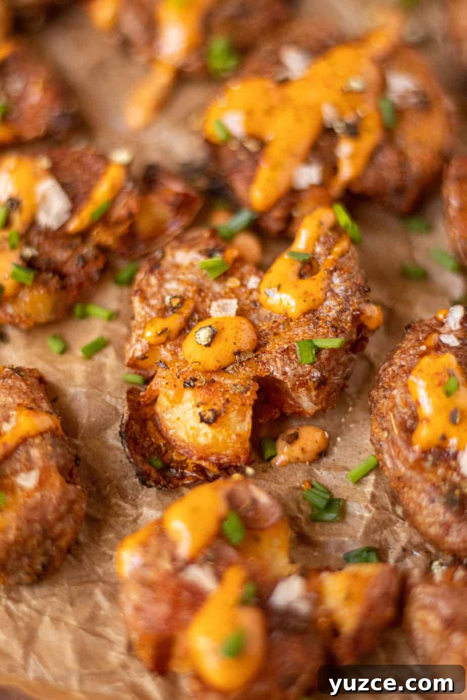 Crispy Smashed Potatoes with Spicy Creole Sauce 3 side angle shot of crispy smashed potatoes with creole sauce on parchment paper.