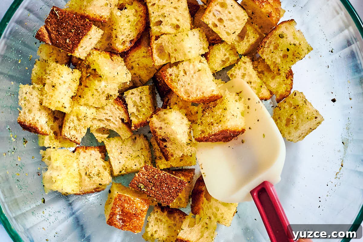 Crispy Air Fryer Crouton Recipe for Salad and Soup 7 Seasoned bread cubes for croutons in a bowl with stirring spoon.
