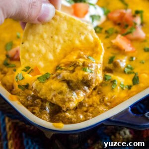 Loaded Beef Enchilada Dip Recipe for Party Appetizers 7 close up scooping enchilada dip out with a chip