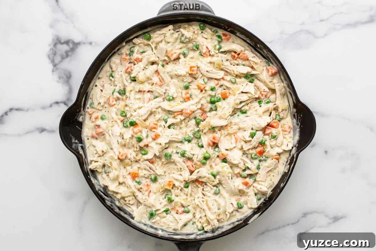 Chicken and frozen veggies in a creamy sauce in a pan. 