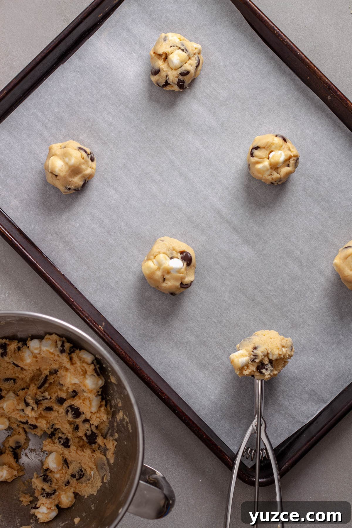 Chewy Chocolate Chip Cookies with Gooey Marshmallow Centers 10 A parchment lined baking sheet with balls of chocolate chips and marshmallow cookie dough.