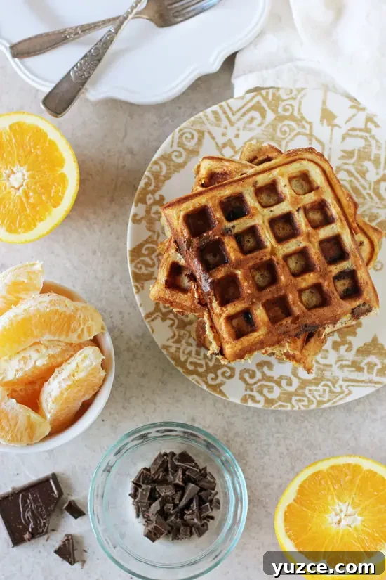 Recipe for orange and dark chocolate waffles. Made with white whole wheat flour and coconut oil! Filled with orange zest and chopped dark chocolate! A plate with Orange Chocolate Waffles and bowls of orange slices and chopped chocolate.