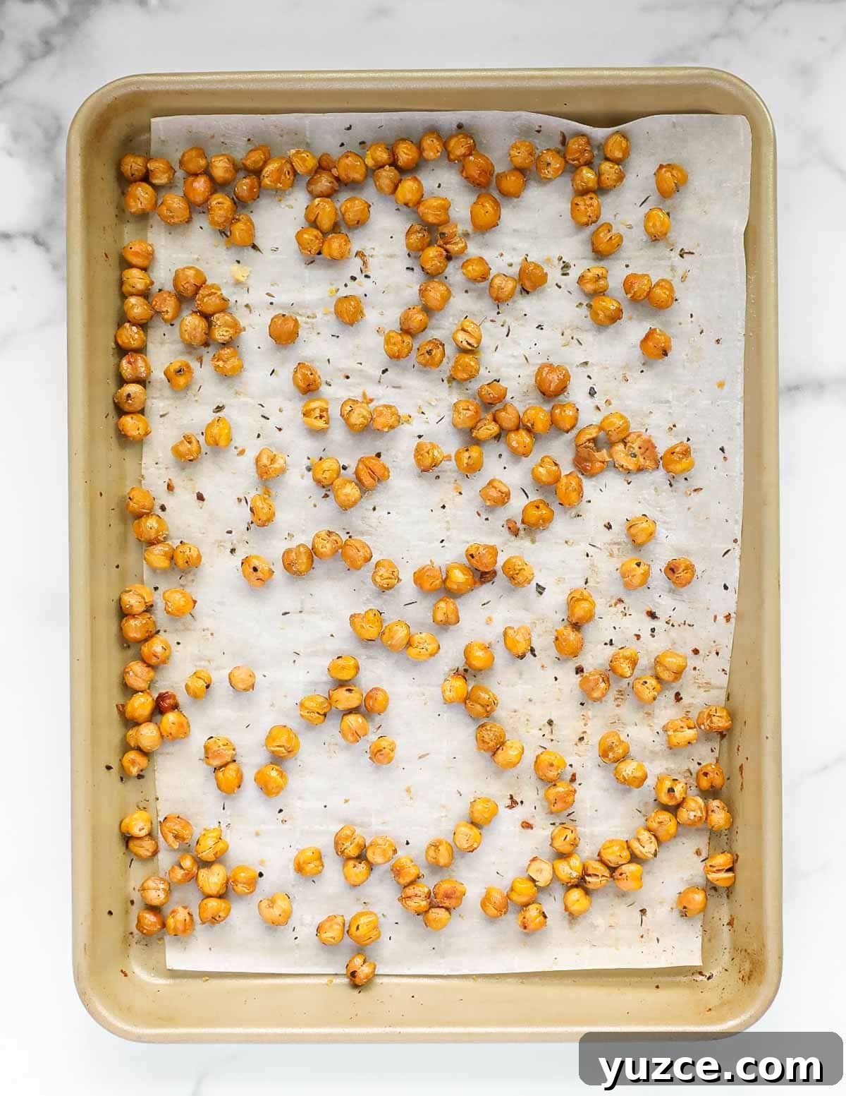Chickpeas spread out on a piece of white parchment paper on a gold backing sheet.